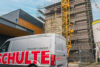 Schulte Servicefahrzeug vor Baustelle mit Kran und Gerüst an mehrstöckigem Backsteingebäude mit Schlosserei im Hintergrund