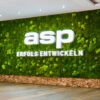 Grüne Mooswand mit weißem asp Logo und Slogan "ERFOLG ENTWICKELN" in moderner Bürolobby